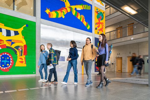 Foto von fünf Studierenden an der TUD, die plaudernd Richtung "Audimax" entlang gehen