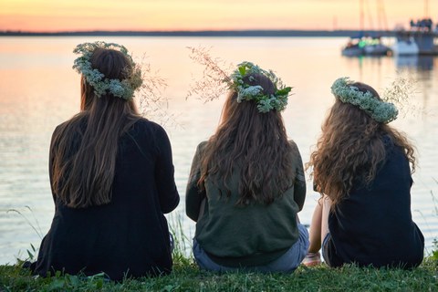 three young women with wreaths of flowers and herbs sitting by the lakeside