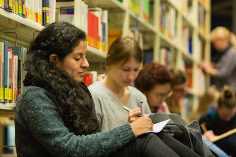 Teilnehmende der LNDS sitzen auf dem Boden der Bibliothek und schreiben mit Stift und Papier.