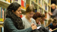 Teilnehmende der LNDS sitzen auf dem Boden der Bibliothek und schreiben mit Stift und Papier.
