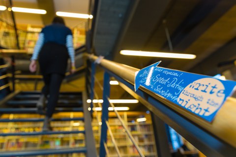Ein nachtblauer Pfeil mit einem gelben Mond weist den Weg die Treppe hinauf zum "SPeed-Dating für Lern- und Schreibgruppen". Im Hintergrund läuft eine Person die Treppe hinauf.