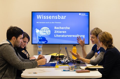 Zwei Mitarbeiterinnen der SLUB beraten zwei Studierende zu den Themen Recherche, Zitieren und Literaturverwaltung. Sie sitzen zu viert an einem Tisch, vor ihnen stehen Laptops.