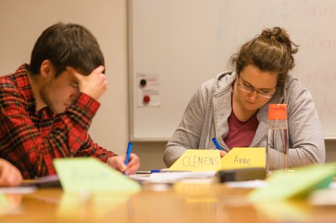 Zwei Studierende sitzen mit gesenkten Köpfen und konzentrierten Blicken über ihren Arbeitspapieren.