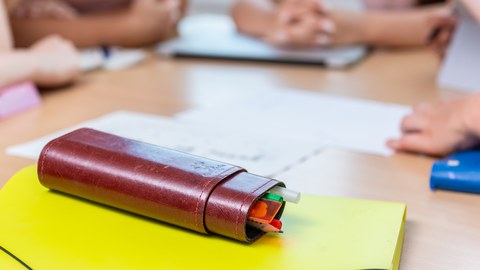 Studierende in einer Workshoprunde, im Vordergrund liegt ein Schreibetui aus Leder