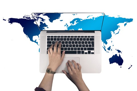 Top view of a laptop with hands on the keyboard. The desktop shows a section of a Eurocentric world map. This section is continued in the background, around the laptop.