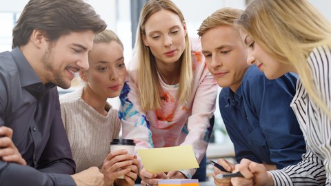The picture is a photo of 5 students looking at a small paper. 