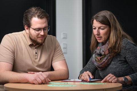 A woman and a man sit facing each other at a round table and talk. They are a student counselor and a client.