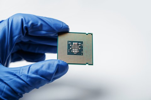 Foto einer blau behandschuhten Hand, die einen Mikrochip in die Kamera zeigt.