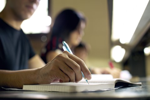 zwei Personen, im Fokus Hand mit Stift auf Notizbuch
