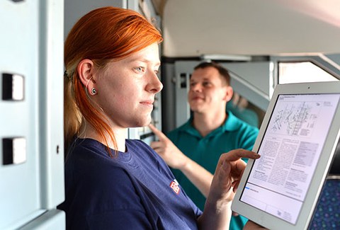 Das Foto zeigt eine Frau, die auf ein Tablet schaut und einen Bauplan studiert. Im Hintergrund erkennt man einen Mann.