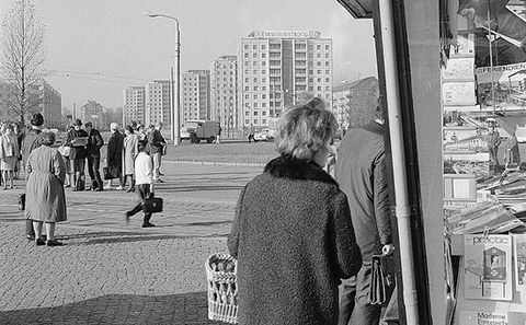 The black-and-white photo depicts Postplatz square in Dresden at an earlier time. Many people and a newspaper stand are visible. Some people wait in line in front of it.