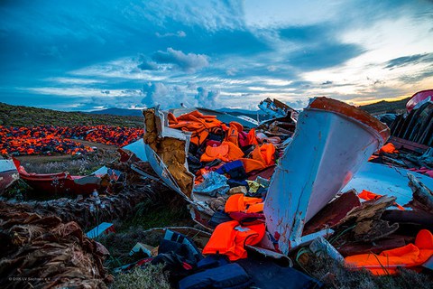 The photo shows multiple wrecked boats on land and many neon orange life vests scattered about.