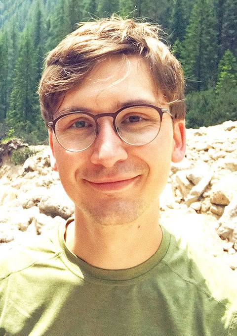 Photo portrait of Felix Socher standing outside in front of some boulders and trees.