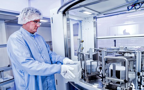 The photo shows Uwe Beier. He is standing and wearing a hairnet, gloves and a coat next to a large machine.