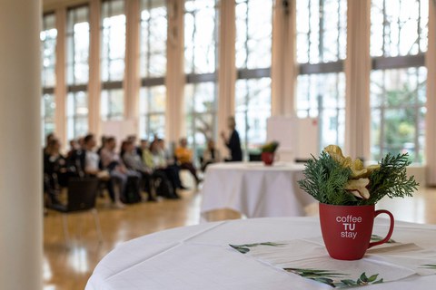 Rechts im Vordergrund eine bepflanzte rote Tasse, im Hintergrund sitzende Teilnehmende