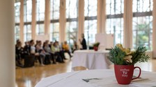 Rechts im Vordergrund eine bepflanzte rote Tasse, im Hintergrund sitzende Teilnehmende