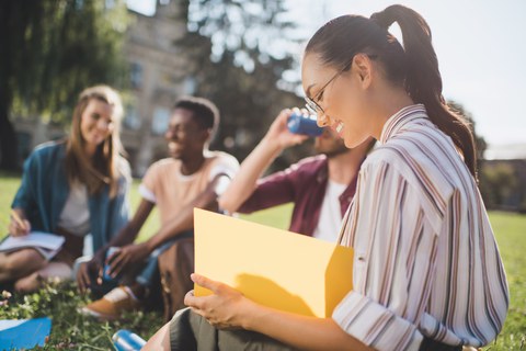 happy international students sitting on a sunny meadow.