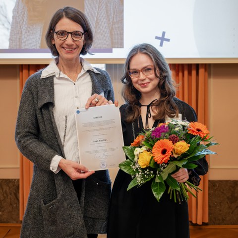 Ms. Costache is standing next to Prof. Dr. Roswitha Böhm, presenting her certificate as well as a bouquet of flowers