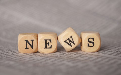 Photo with four wooden cubes lying on a printed sheet of paper. On each cube is a letter. The letters make the word "News".