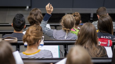 Studierende in einer Vorlesung im Hörsaal, eine Studierende meldet sich