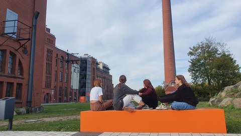 Vier Mädchen sitzen vor einem Industriegebäude aus Backstein.