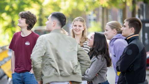 Eine gruppe Jugendlicher und ein Erwachsener stehen draussen zusammen.