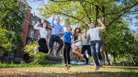 Six students jump into the air in front of the Beyer Building of the TU Dresden