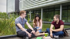 Studierende sitzen am Teich des Informatikgebäudes