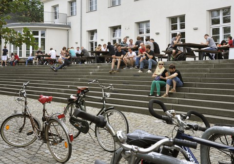 Studierende sitzen auf den Stufen vor der Mensa.