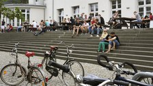 Studierende sitzen auf den Stufen vor der Mensa.