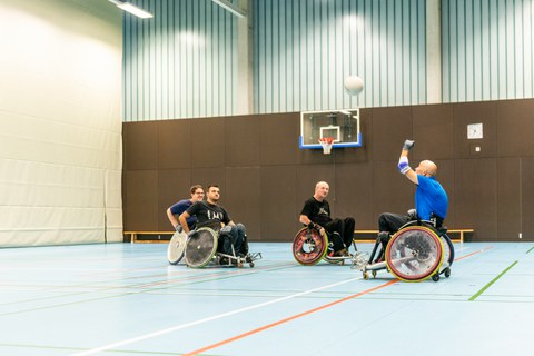 Foto: Vier Rollstuhlfahrer spielen Rugby in einer großen Sporthalle der TU Dresden. 