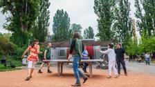 Foto: Eine Gruppe von sechs fröhlichen Studierenden spielt Tischtennis vor dem Grill Cube am Hörsaalzentrum. im Hintergrund sind Bäume zu erkennen.