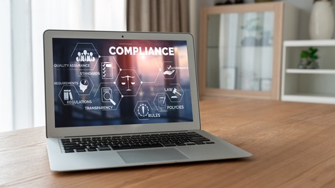 Foto: Ein Laptop steht auf dem Tisch, das Display ist gut lesbar und zeigt einre Grafik mit der Aufschrift "Compliance".