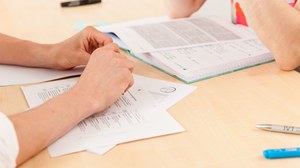 Close-up of a desk. Two people are sitting opporsite each other with textbooks and notes open in front of them.