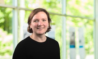 Porträtfoto von Antje Döschner. Sie trägt halblange offene Haare, die hinter dem Ohr stecken und ein schwarzes Oberteil
