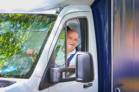 Foto eines TUD-Mitarbeiters, der als Fahrer tätig ist. Er schaut lachend aus seinem Autofenster.enster