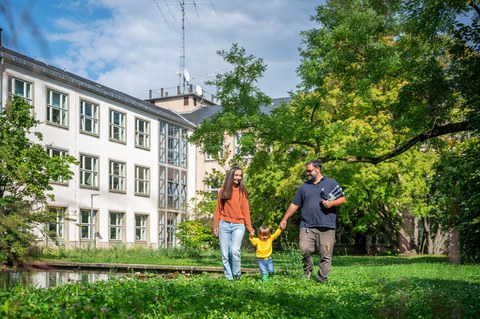 Foto eines Paares mit einem Kleinkind an den Händen, die über den TU Dresden Campus laufen