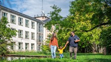 Foto eines Paares mit einem Kleinkind an den Händen, die über den TU Dresden Campus laufen