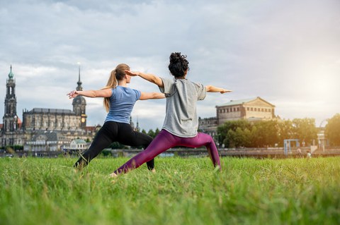 Foto zeigt zwei Studentinnen von hinten, die an der Elbe Yoga machen.