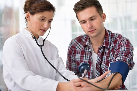 Auf dem Foto ist zu sehen, wie eine Ärztin den Blutdruck bei einem jungen Mann misst.