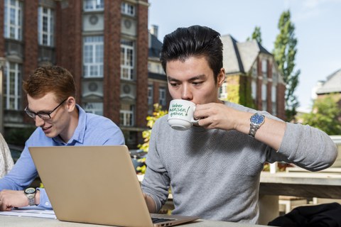 Foto eines Studierenden, der im Freien einen Kaffee trinkt