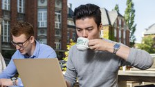 Foto eines Studierenden, der im Freien einen Kaffee trinkt