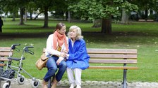 Foto einer jüngeren und älteren Frau, die beide auf einer Bank sitzen.