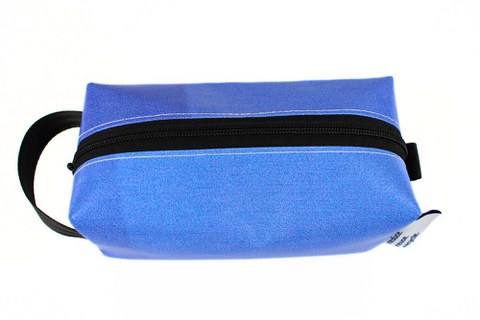 You can see a view of a cuboid bag with a zipper on the top. On the left side there is a black carrying strap made from a car belt.