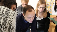 Foto der Teamarbeit. Studierende stehen beisammen und schauen auf etwas hinab, das sich außerhalb des Fotos befindet.