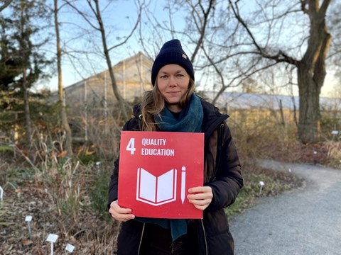 Eine Frau die eine rote Karte mit der weißen Aufschrift 4 Quality Education in den Händen hält. 