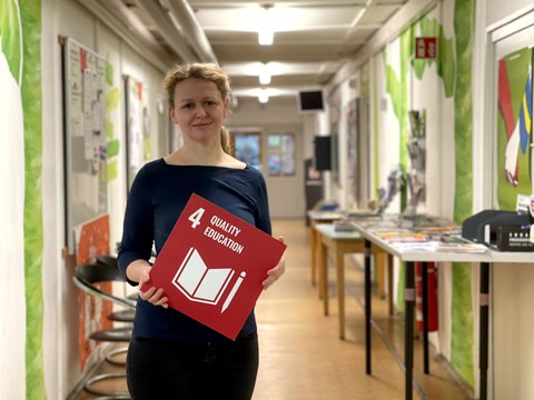 Eine Frau die eine rote Karte mit der weißen Aufschrift 4 Quality Education in den Händen hält.