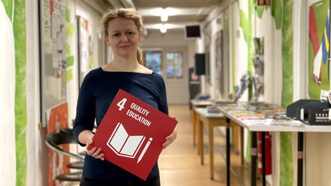 Eine Frau die eine rote Karte mit der weißen Aufschrift 4 Quality Education in den Händen hält.