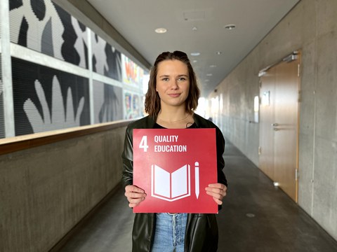Eine Frau die eine rote Karte mit der weißen Aufschrift 4 Quality Education in den Händen hält.