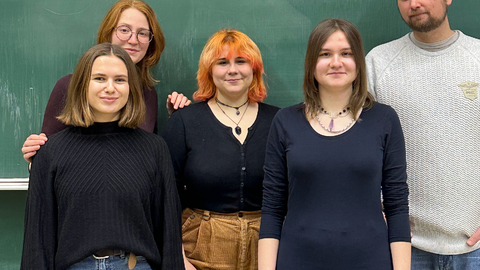 Photo of students and a lecturer standing in front of a blackboard on which the word "Sustainability" is written in green chalk